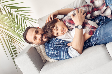 Father and little son at home lying on sofa hugging looking camera cheerfulの写真素材
