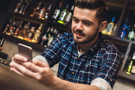 Young bartender leaning on bar counter browsing internet joyful close-upの写真素材
