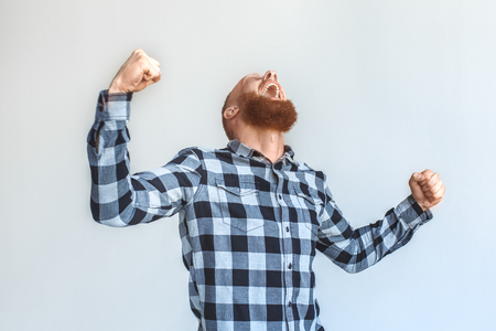 Freestyle. Mature man standing isolated on grey keeping hands in fists up shouting cheerfulの写真素材