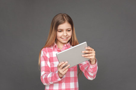 Freestyle. Girl standing isolated on grey playing game on digital tablet joyfulの写真素材