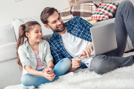 Father and little daughter at home sitting browsing internet online shopping smilingの写真素材