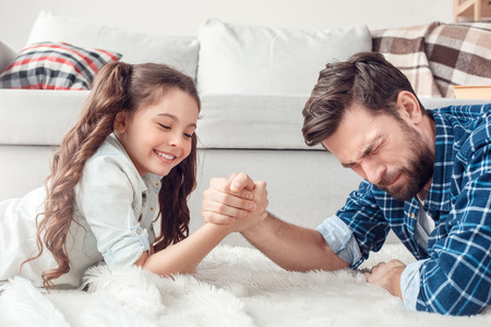 Father and little daughter at home lying on floor fighting playfulの写真素材