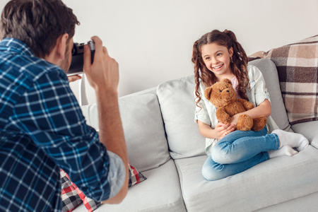 Father and little daughter at home man taking photos of daughter with teddy bear happyの写真素材