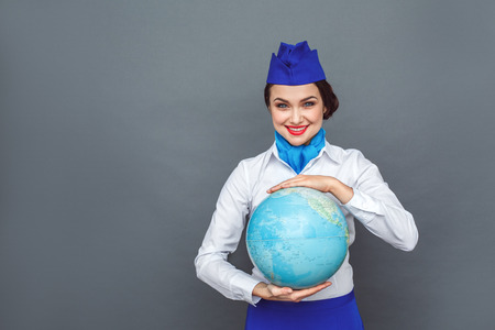 Professional Occupation. Stewardess standing isolated on grey with globe looking camera smiling excitedの写真素材