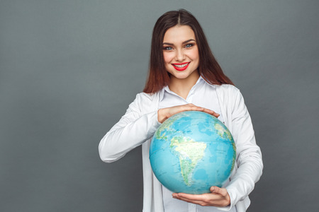 Freestyle. Woman standing isolated on grey with globe smiling joyfulの写真素材