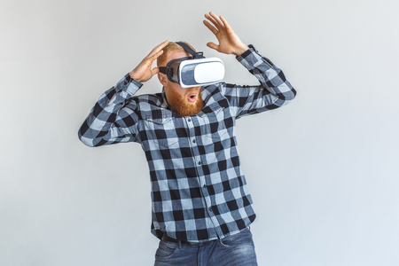 Freestyle. Mature man in virtual reality headset standing isolated on grey playing hands up surprisedの写真素材