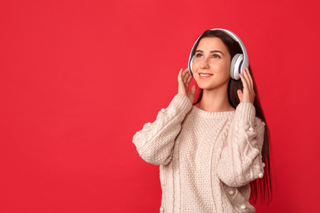 Freestyle. Young woman in headphones standing isolated on red listening music looking up smiling happyの写真素材