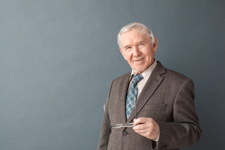 Senior man studio standing isolated on gray holding glasses looking camera joyfulの写真素材