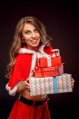 Christmas and New Year. Woman in santa costume standing isolated on black with presents looking camera surprisedの写真素材
