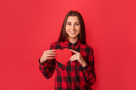 Valentines Day. Young woman standing isolated on red with heart card smiling happy to cameraの写真素材