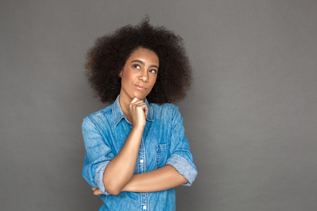 Freestyle. Mulatto woman standing isolated on grey looking aside thoughtfulの写真素材