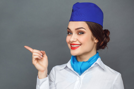 Professional Occupation. Stewardess standing isolated on grey pointing aside smiling confidentの写真素材