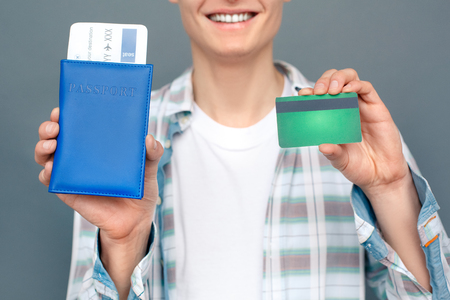 Man isolated on gray wall tourism concept standing holding passport with ticket and debit card close-up happyの写真素材