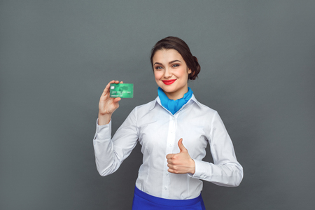 Professional Occupation. Stewardess standing isolated on grey with credit card showing thumb up smiling positiveの写真素材