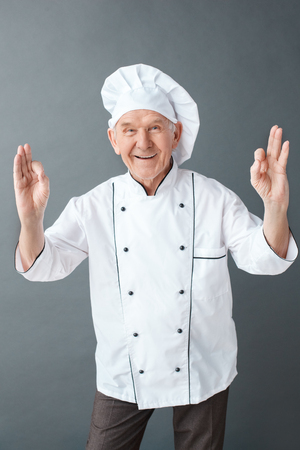 Senior chef studio standing isolated on gray smiling cheerful showing ok signの写真素材