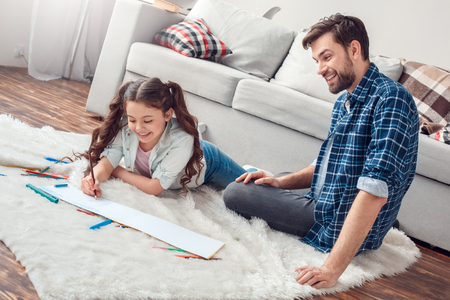 Father and little daughter at home on floor man looking at daughter drawing in album smilingの写真素材