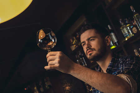 Young bartender standing at bar counter checking glass cleanlinessの写真素材