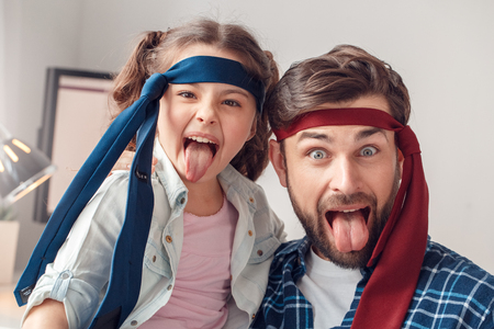 Father and little daughter at home sitting wearing ties tongue out grimaceの写真素材