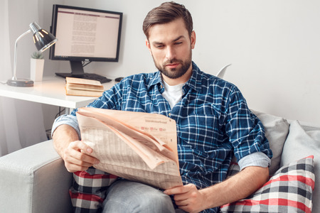 Young man leisure at home sitting reading newspaper relaxedの写真素材