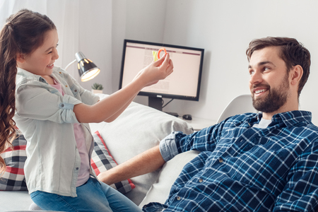 Father and little daughter at home sitting girl offering father to make hairstyle playfulの写真素材