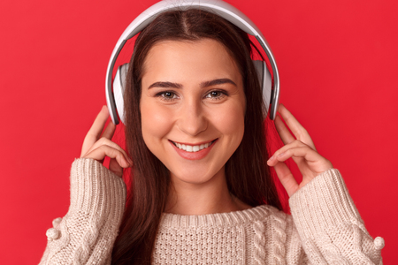 Freestyle. Young woman in headphones standing isolated on red listening music smiling toothy to camera close-upの写真素材