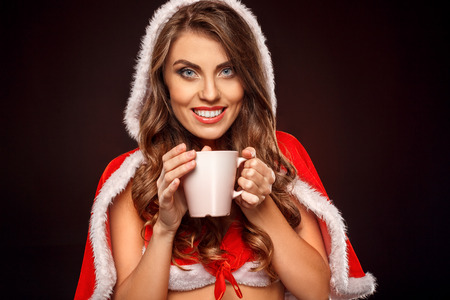 Christmas and New Year. Woman in santa costume standing isolated on black drinking hot milk smiling happy close-upの写真素材