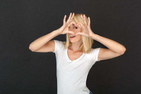 Freestyle. Woman standing isolated on black wall looking through the heart shape to camera playfulの写真素材
