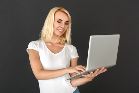 Freestyle. Woman standing isolated on black wall browsing laptop joyfulの写真素材