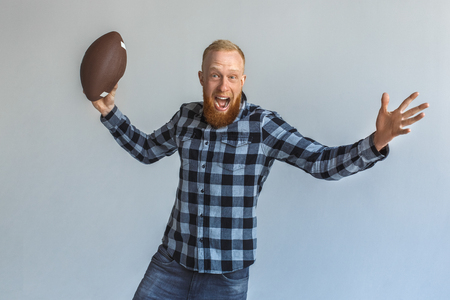 Freestyle. Mature man standing isolated on grey throwing ball shouting excitedの写真素材