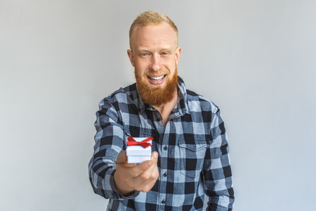 Freestyle. Mature man standing isolated on grey giving small gift to camera smiling happyの写真素材