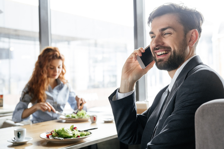Businesspeople having business lunch at restaurant sitting man talking on smartphone close-up while woman eating saladの写真素材
