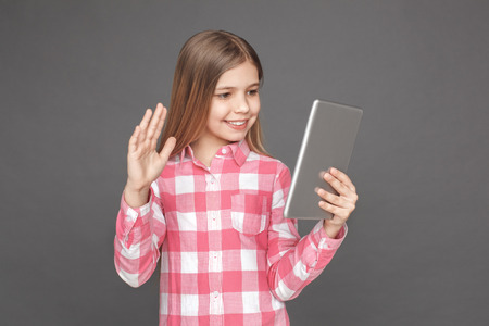 Freestyle. Girl standing isolated on grey having video call on digital tablet smiling friendlyの写真素材