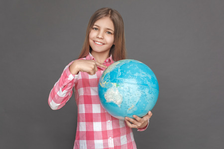 Freestyle. Girl standing isolated on grey pointing at destination on globe smiling happyの写真素材