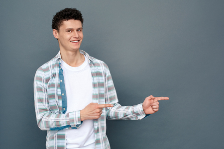 Man isolated on gray wall free style standing pointing aside looking camera joyfulの写真素材
