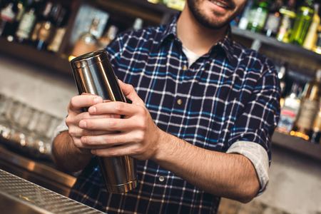 Young bartender standing at bar counter mixing drink close-up happyの写真素材