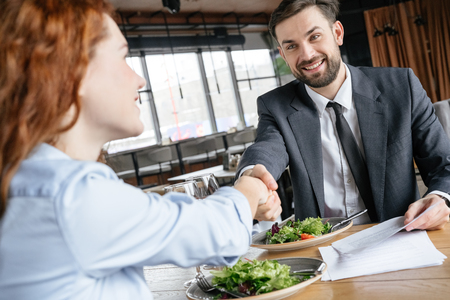 Businesspeople having business lunch at restaurant sitting eating salad drinking wine shaking hands making deal happyの写真素材