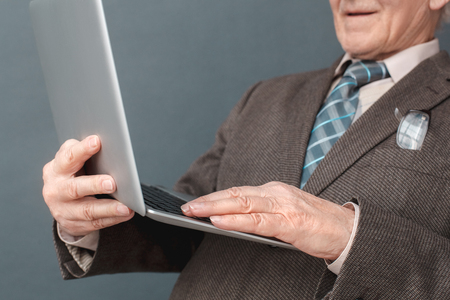 Senior man studio standing isolated on gray using laptop checking media smiling close-upの写真素材