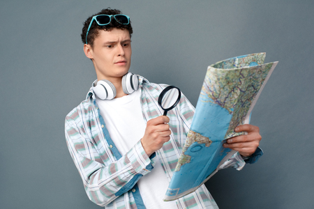 Man isolated on gray wall tourism concept standing magnifying map thoughtfulの写真素材