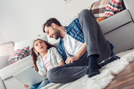 Father and little daughter at home sitting man looking at daughter with laptop concernedの写真素材