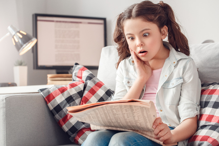 Little girl leisure at home sitting reading news shockedの写真素材