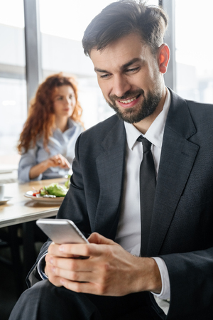 Businesspeople having business lunch at restaurant sitting man close-up browsing smartphone while woman eating behindの写真素材