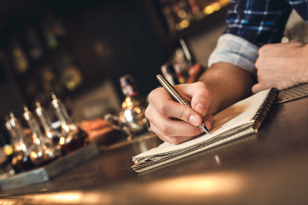 Young barman standing at bar counter taking notes to do list close-up blurred backgroundの写真素材