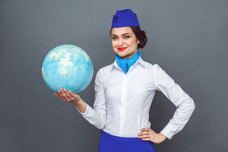 Professional Occupation. Stewardess standing isolated on grey showing globe looking camera confidentの写真素材