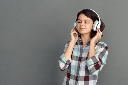 Freestyle. Young woman in headphones isolated on grey listening music closed eyes joyfulの写真素材