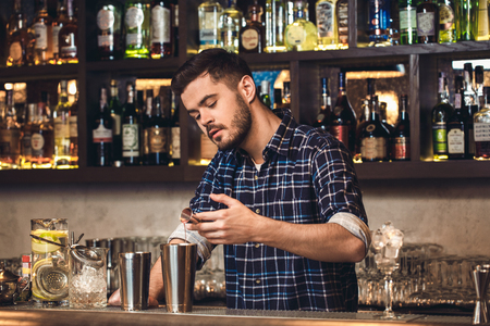 Young bartender standing at bar counter pouring ingredient into shaker concentratedの写真素材