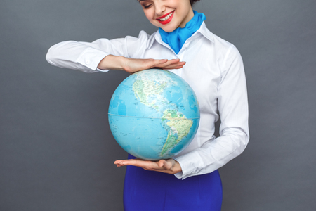 Professional Occupation. Stewardess standing isolated on grey looking at destination on globe close-up smiling joyfulの写真素材
