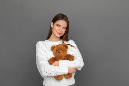 Freestyle. Young girl standing isolated on grey hugging teddy bear smiling happyの写真素材