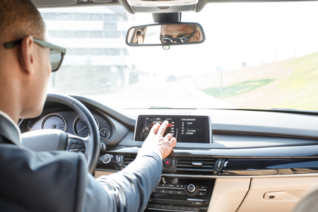 Young businessman driver in sunglasses sitting inside car driving choosing destination on navigator back seat viewの写真素材