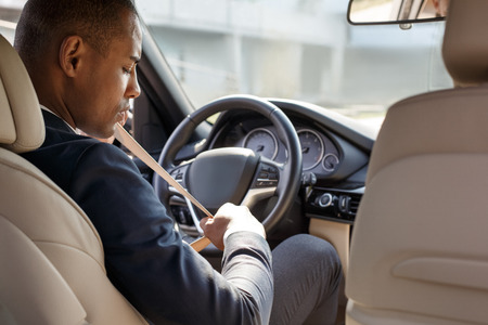 Young businessman driver sitting inside car fastening belt back seat viewの写真素材