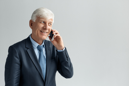 Business Lifestyle. Businessman standing isolated on gray talking on smartphone smiling playfulの写真素材